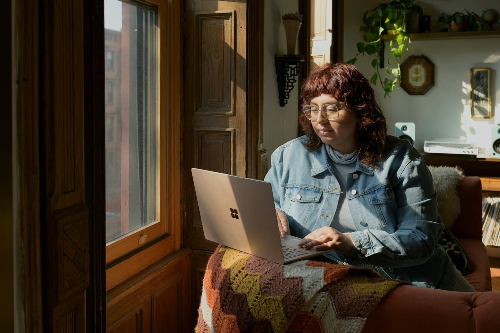 Person working on a laptop on a sofa at home by a sunny window